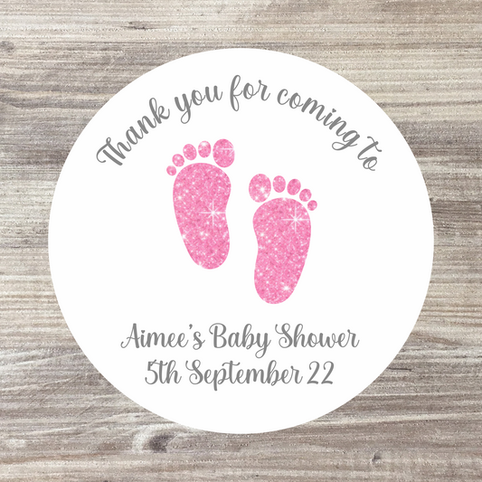 A white sticker with 2 pink glitter effect footprints in the middle and grey writing above and below reading, thank you for coming to aimee's baby shower, 5th September 2022
